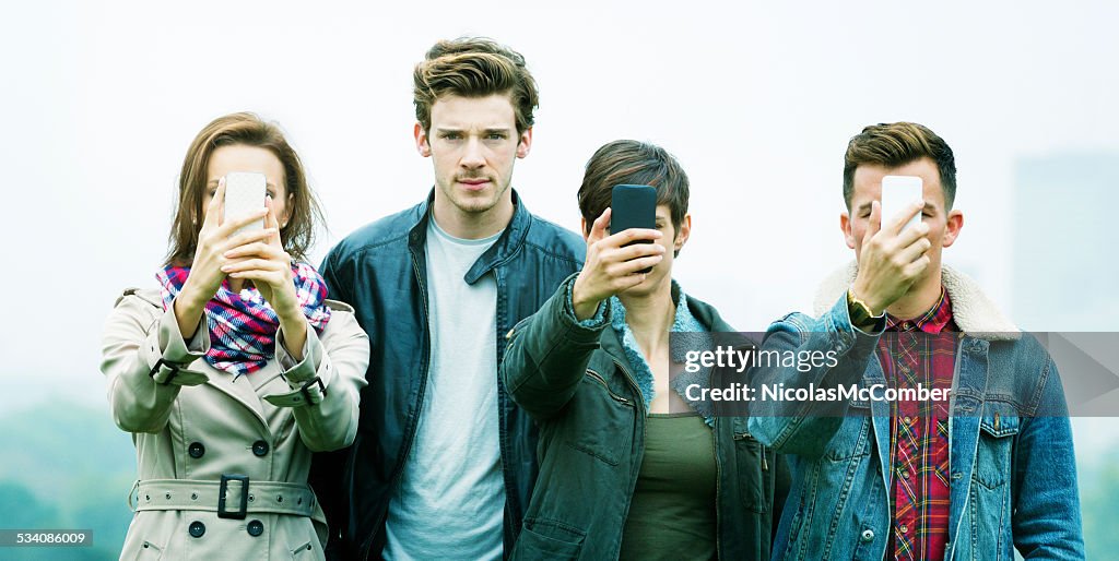 Young man frowns as friends are obsessed with phones