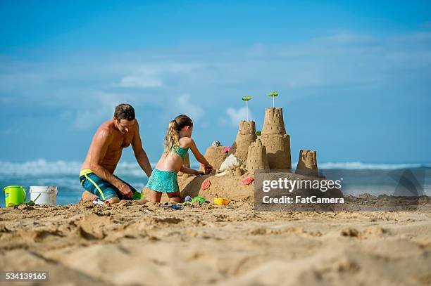 father and daughter family building sand castle on beach - zandkasteel stockfoto's en -beelden