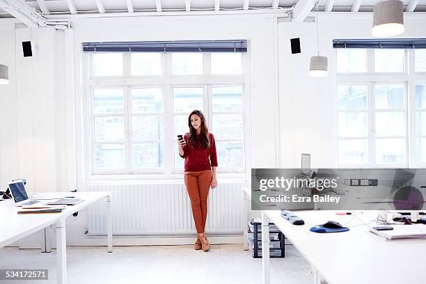 woman texting in modern open plan office - person standing front on inside stock pictures, royalty-free photos & images