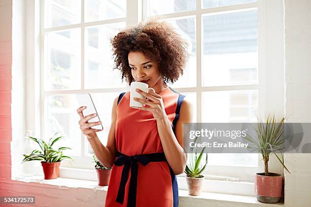 woman drinking coffee and checking her phone - orange dress stock-fotos und bilder