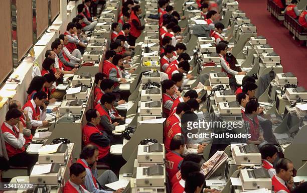 Stock traders crowd telephones, computers, and themselves along tables on the trading floor of the Hong Kong Stock Exchange.