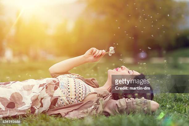 donna rilassante nel parco che soffia dente di leone - sognare ad occhi aperti foto e immagini stock