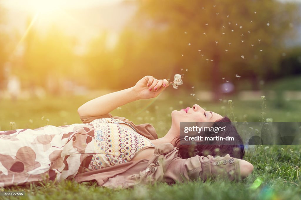 Relaxed woman in the park blowing dandelion