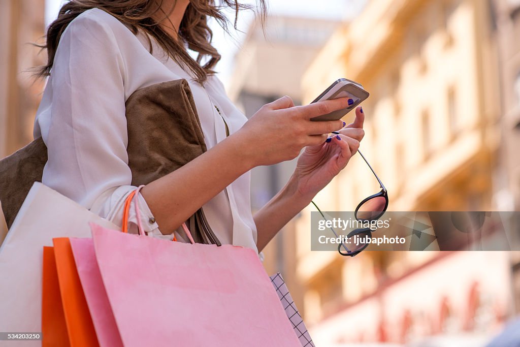 Frauen tragen von Shopping Taschen und er ein smartphone benutzt