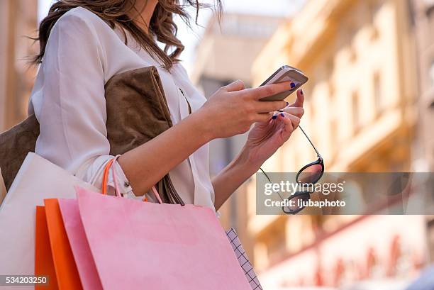 frauen tragen von shopping taschen und er ein smartphone benutzt - shopping bag stock-fotos und bilder