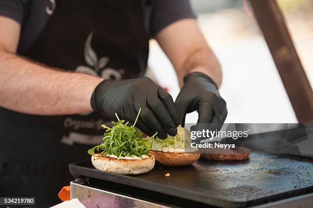preparing hamburger with arugula outdoors - zwarte handschoen stockfoto's en -beelden