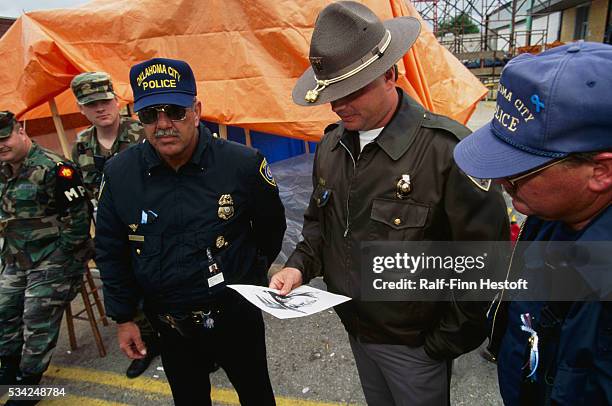 Oklahoma City police officers study a sketch of a suspect while military police stand by on the site of the Oklahoma City bombing. On April 19th a...