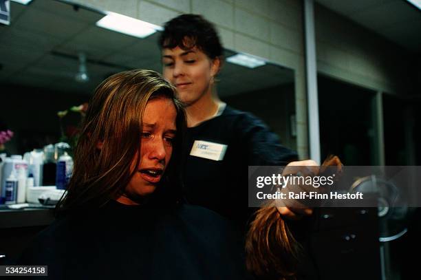 Navy recruit looks sadly at a handful of her freshly cut hair as a hairstylist trims her hair to Navy specifications. The new recruit is training at...