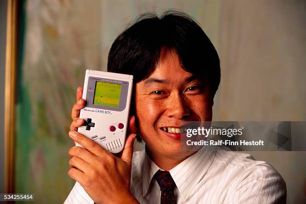 Shigeru Miyamoto, creator of Mario and other characters and video games for Nintendo, holds a Nintendo Game Boy containing the Super Mario World...