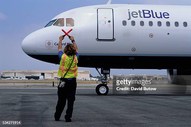 An aircraft maintenance crew personnel guides an arriving JetBlue flight on the tarmac at Long Beach Airport.