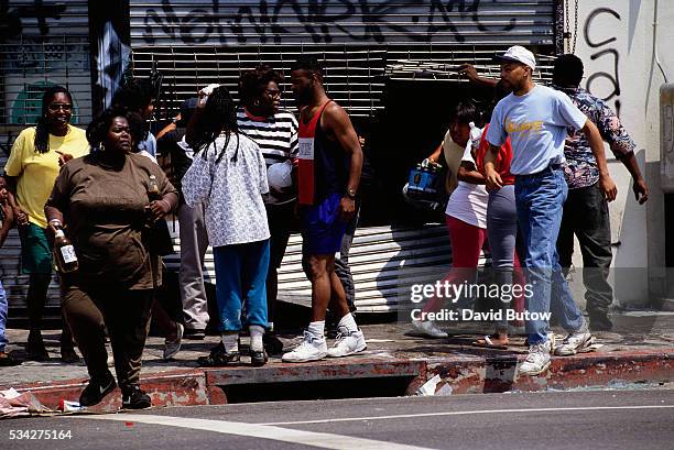Pedestrians walk past damaged buildings following the Los Angeles riots. In April of 1992, after a jury acquitted the police officers involved in the...