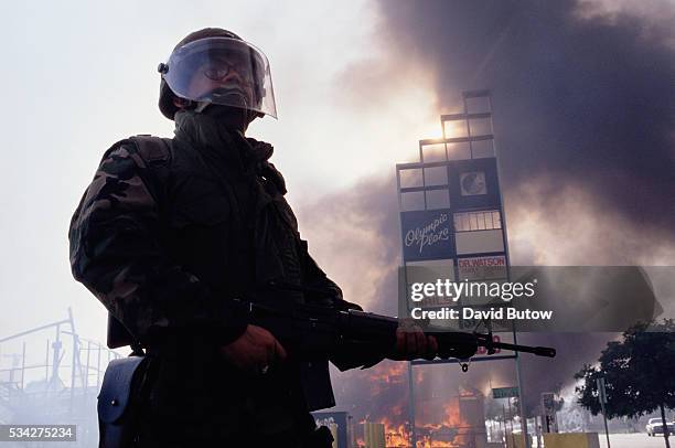 Member of the National Guard stands near burning building during the Los Angeles riots. In April of 1992, after a jury acquitted the police officers...
