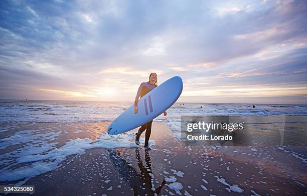 beautiful middle aged female surfer on beach at dusk - surfer wetsuit stock pictures, royalty-free photos & images