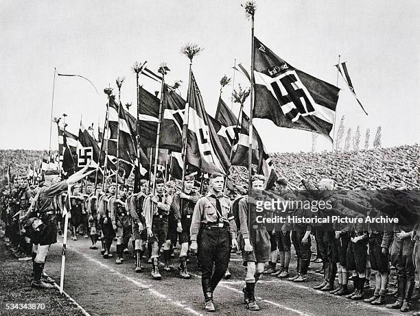 "Hitler Youth rally on National Socialist Party Day saluting and carrying Nazi flags. "