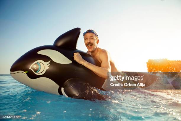 man playing on a inflated whale - very tanned man stock pictures, royalty-free photos & images