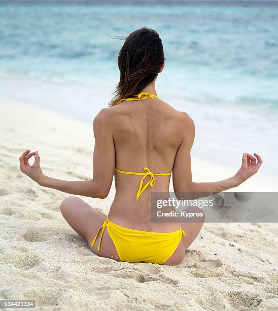 asia, maldives, view of young caucasian woman wearing yellow bikini on tropical beach sitting on the sand thinking in yoga position - frau meditation stock pictures, royalty-free photos & images
