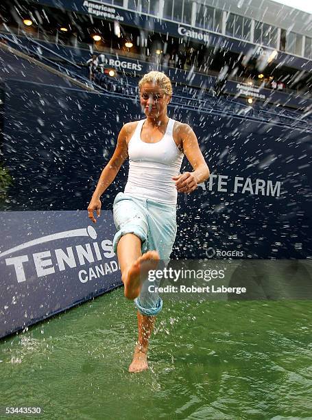 Kim Clijsters of Belgium kicks water at photographers on center court after torrential rains delayed play during the match between Amelie Mauresmo of...