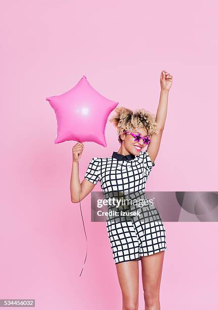 afro american young woman holding pink star foil balloon - sunglasses isolated stockfoto's en -beelden