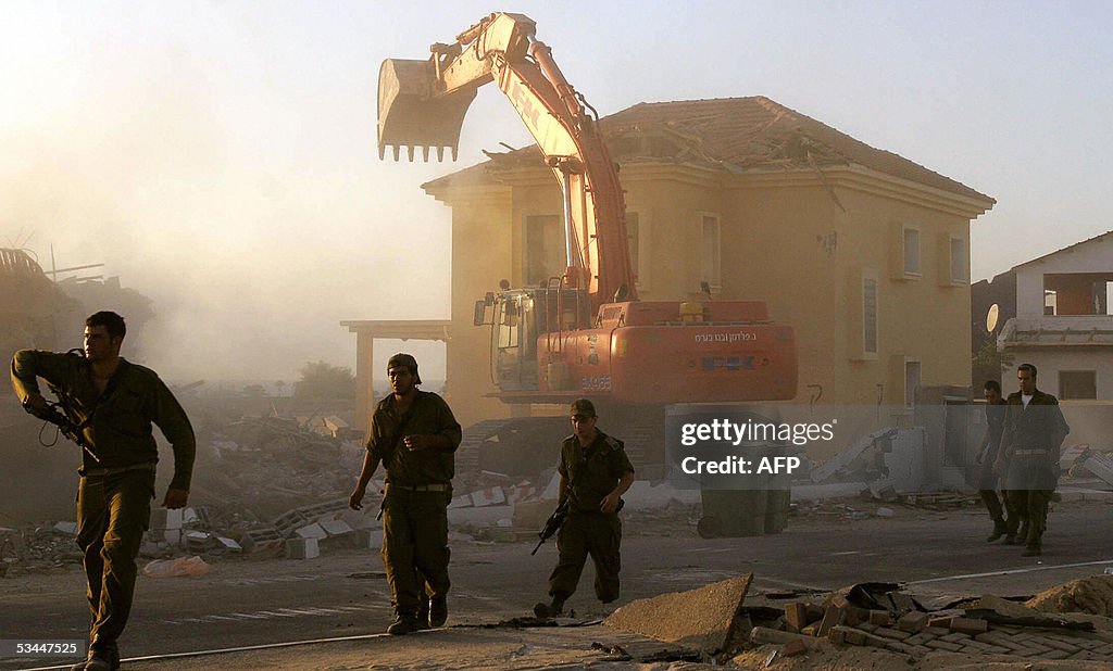 Israeli soldiers walk past a bulldozer d