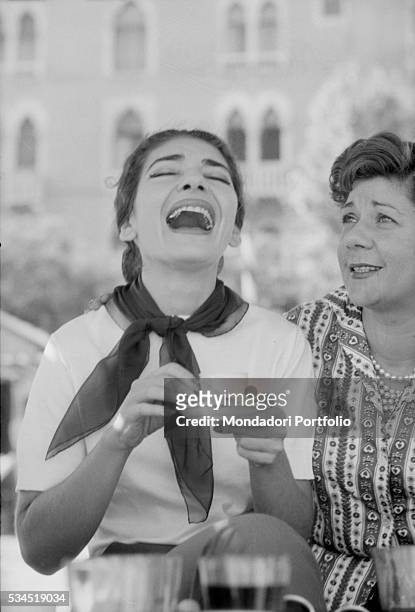 Greek soprano Maria Callas laughing with a cup of coffee next to Italian countess Anna di Castelbarco during the XVIII Venice International Film...