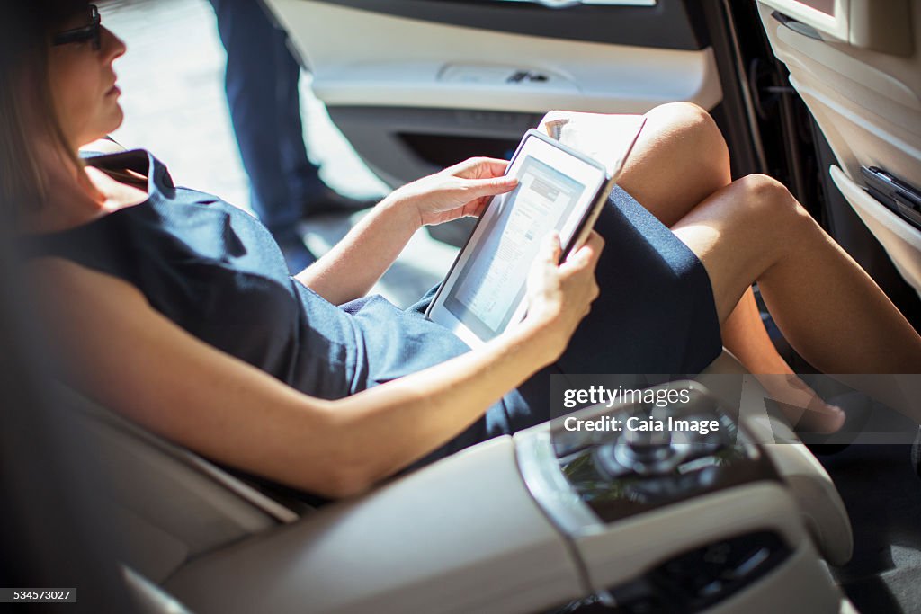 Businesswoman using digital tablet in back seat of car