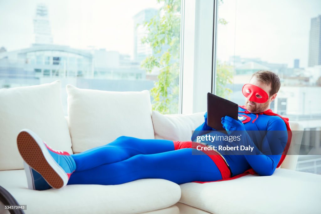 Superhero using digital tablet on living room sofa