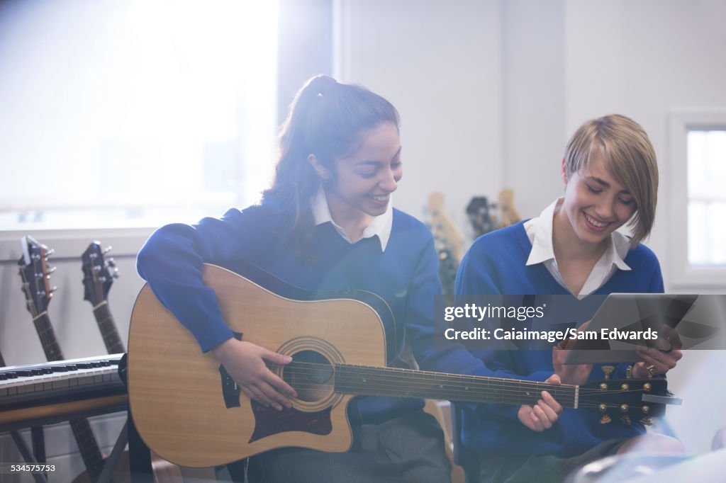 Female students playing acoustic guitar in classroom and using tablet pc