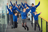Enthusiastic high school students wearing school uniforms smiling and jumping in school corridor