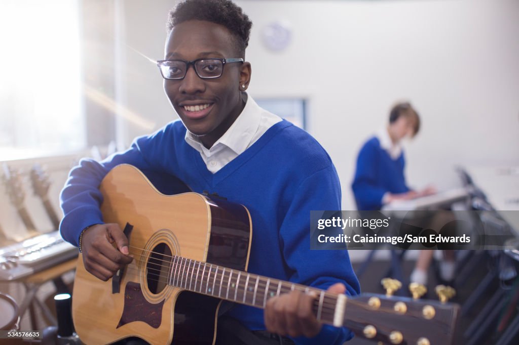 Ritratto di studente maschio sorridente che suona la chitarra acustica in classe