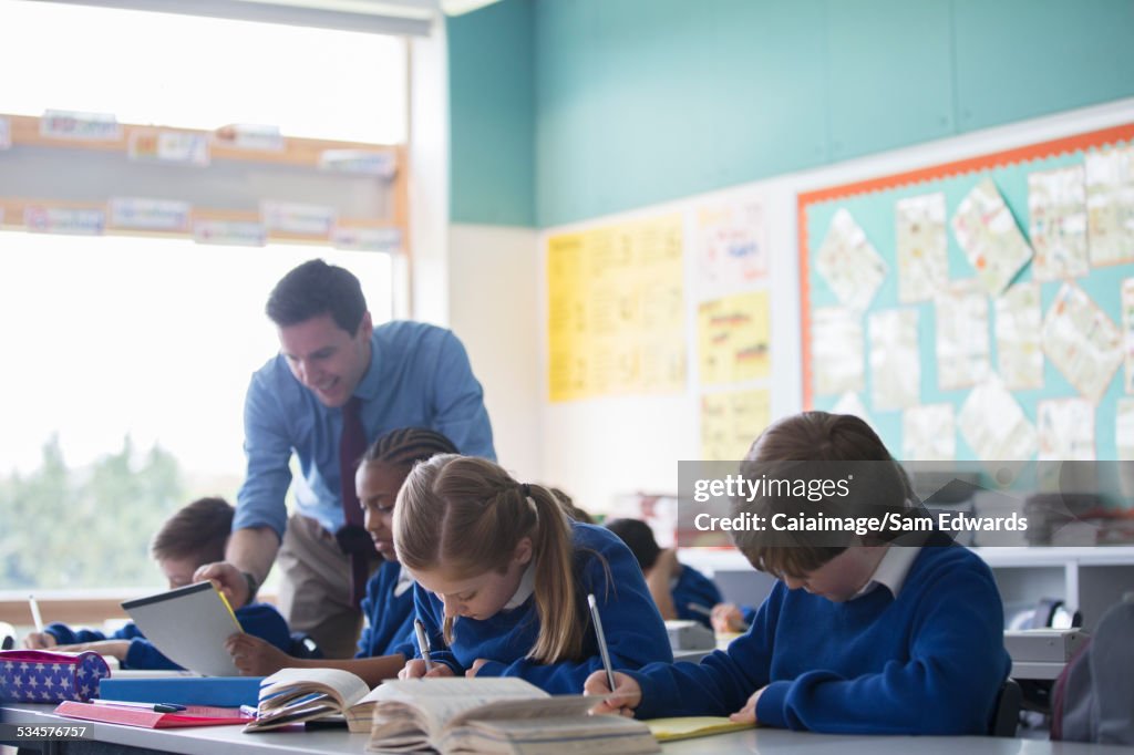 Male teacher assisting elementary school children in classroom during lesson