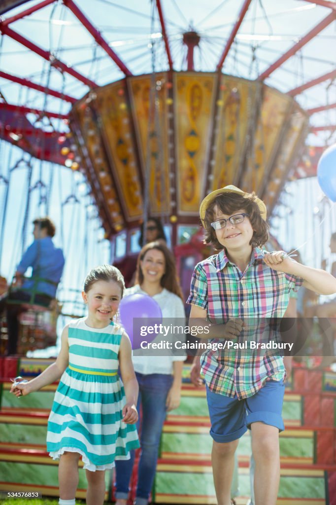 Children running in front of carousel, mother following them
