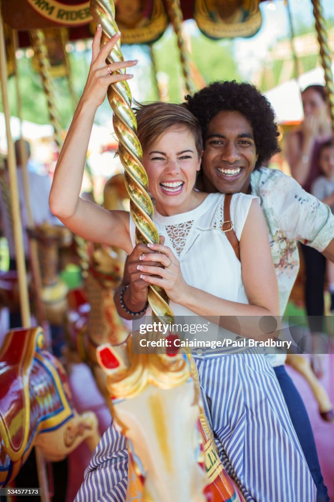 Joven pareja multirracial sonriendo en carrusel en parque de atracciones
