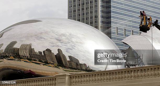 With Chicago's skyline reflected on its steel shell, workers hose down the 110-ton, stainless steel Bean, also called "Cloud Gate" sculpture at...