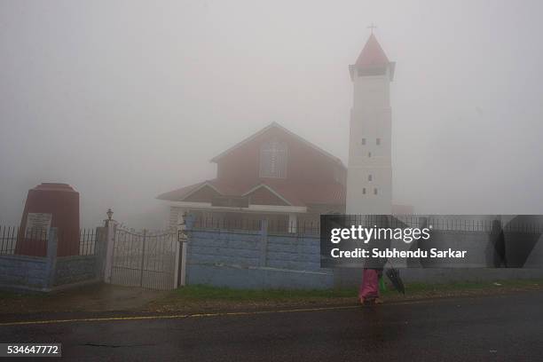 Woman walks with an umbrella along a road in the mist covered Cherapunjee in Meghalaya. Cherrapunjee or Charrapunji is a subdivisional town in the...