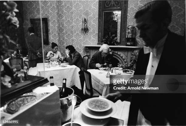 Couples dine in front of a marble fireplace while a waiter prepares a bowl of soup in the private dining room, Le Grand Salon, at French restaurant...