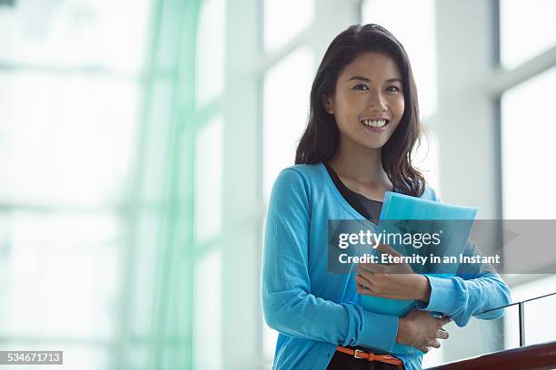 woman holding folders next to a window - blue sweater stockfoto's en -beelden