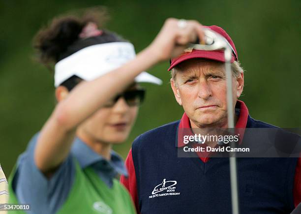 Michael Douglas of the USA watches his wife Catherine Zeta-Jones of Wales choose her club during the Nearest the Pin Charity Challenge prior to the...