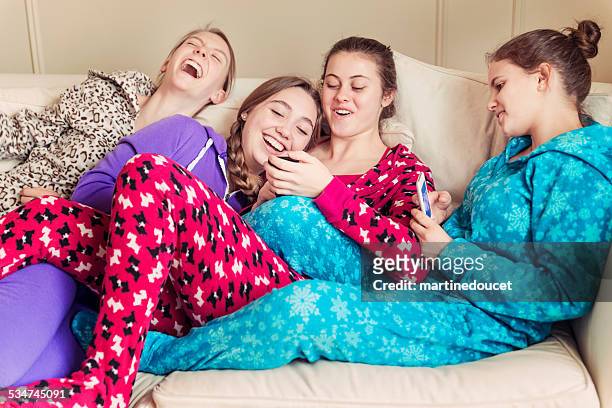 girlfriends wearing onesies laughing on a couch with mobile phones. - babygro stock pictures, royalty-free photos & images