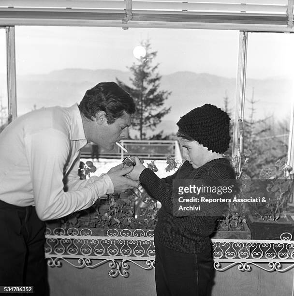His daughter Barbara lighting a cigarette for his father and Italian actor Marcello Mastroianni touching h's chin during their holiday in a village...
