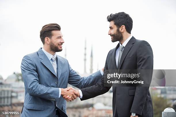 happy businessmen shaking hands in istanbul against clear sky - arab businessman stock pictures, royalty-free photos & images