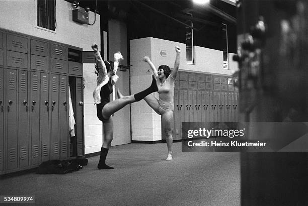 Two Wilde Lake High School students, both in leotards and with their arms raised, kick their legs out beside a bay of hallway lockers after a...
