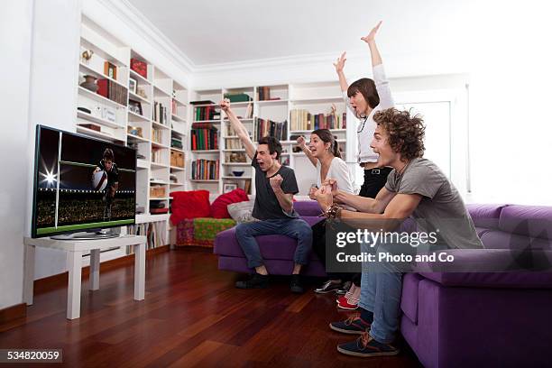 friends watching tv indoors exulting - watching tv sofa stock-fotos und bilder