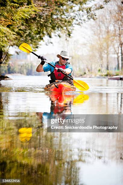 man paddles kayak in tranquil water - snickerdoodle stock-fotos und bilder