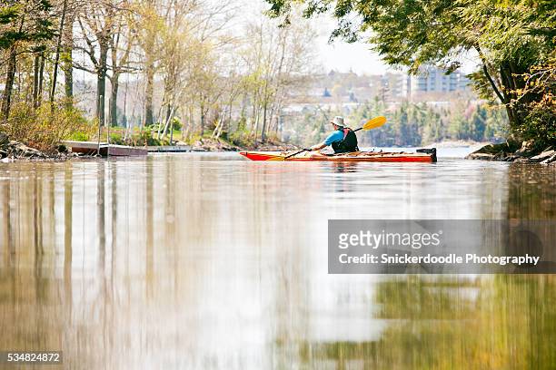 man paddles kayak in tranquil water - snickerdoodle stock-fotos und bilder