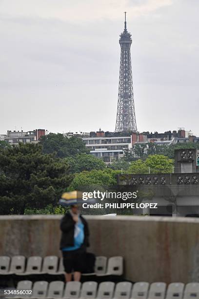 The Eiffel Tower is seen in the background as a woman holding an umbrella leaves the stands after rain interrupted play during the women's third...