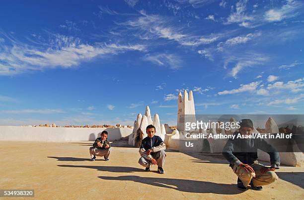 A group of young Algerian boys pausing for a photograph, squatting, in front of the small walls marking the entrance to Melika's cemetery in the...