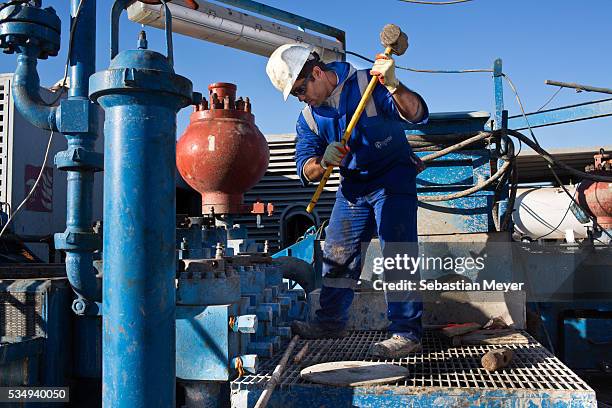 Roustabout closes a valve nut with a sledgehammer on an oil rig.