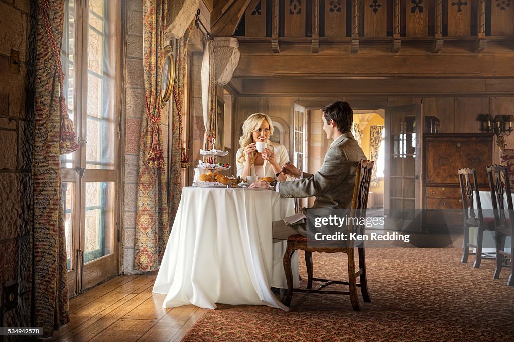 Young couple having tea at small table in front of large French doors in castle