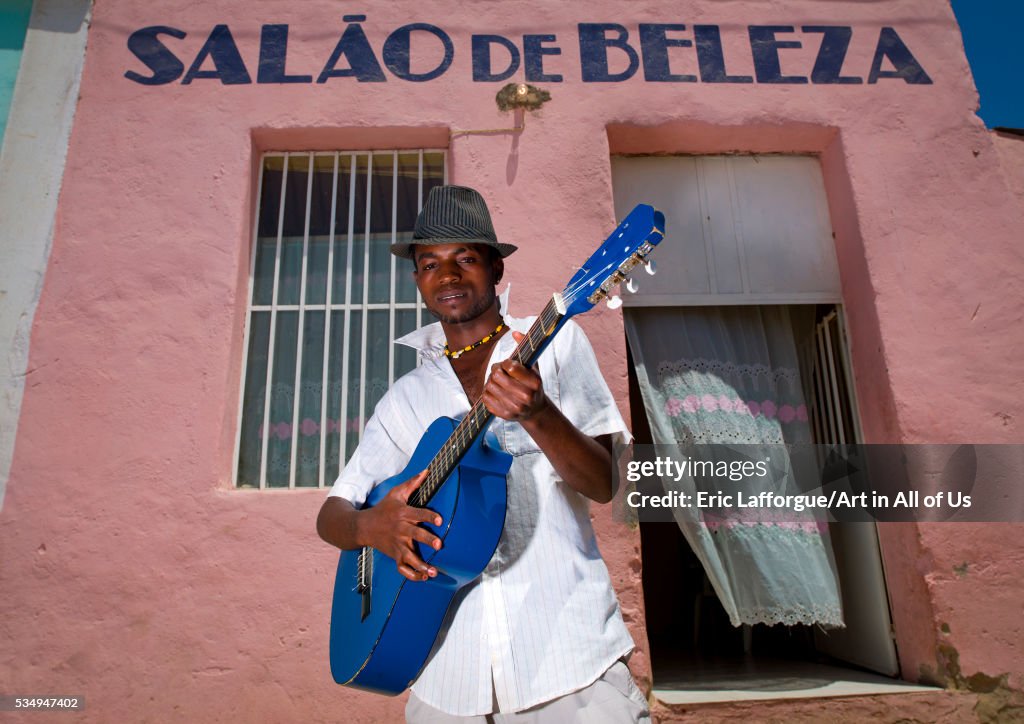 Angola, Southern Africa, Namibe, man with hat playing guitar in front of a beauty salon