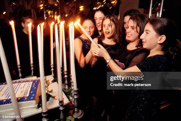 Group of adolescent girls helps their friend Ali Green light candles at her bat mitzvah celebration. The reception takes place at a ballroom on...